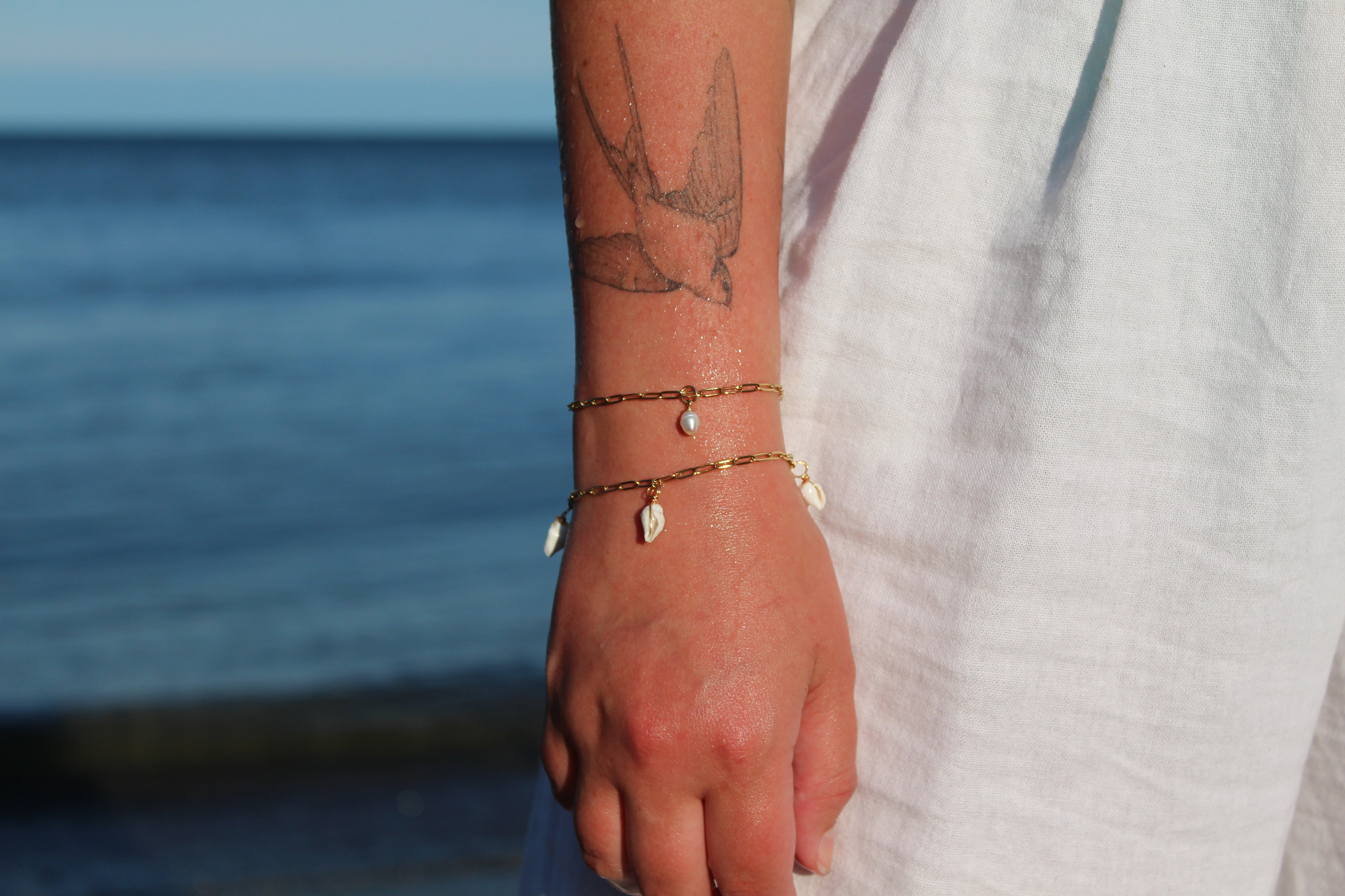 18K gold-plated waterproof tarnish-free paperclip chain bracelets, one with a single pearl, one with 3 mini seashells, handmade and woman owned by CHRMD.